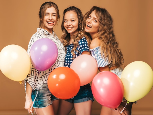 Tre belle donne sorridenti in abiti a scacchi estate camicia. Ragazze in posa Modelli con palloncini colorati. Divertirsi, pronti per la festa di compleanno
