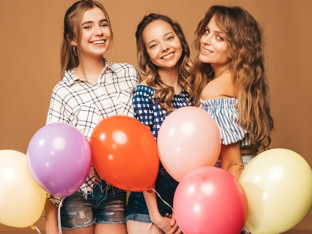 Tre belle donne sorridenti in abiti a scacchi estate camicia. Ragazze in posa Modelli con palloncini colorati. Divertirsi, pronti per la festa di compleanno