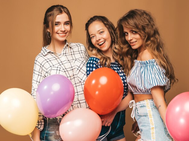 Tre belle donne sorridenti in abiti a scacchi estate camicia. Ragazze in posa Modelli con palloncini colorati. Divertirsi, pronti per la festa di compleanno