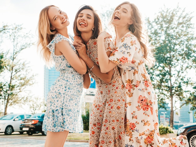 Tre belle ragazze sorridenti in prendisole alla moda estate in posa sulla strada