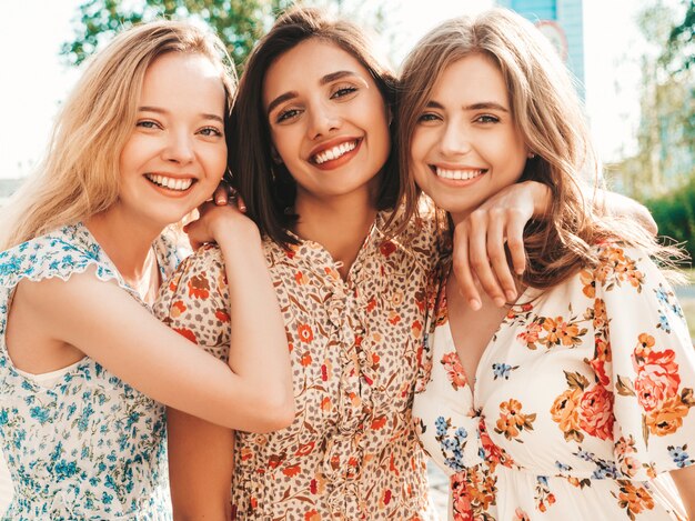 Tre belle ragazze sorridenti in prendisole alla moda estate in posa sulla strada