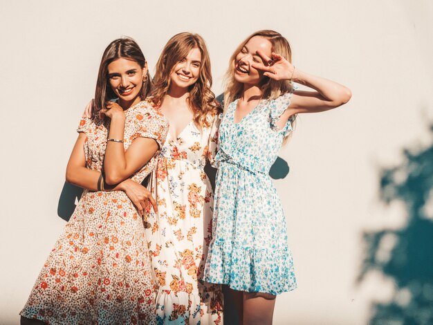 Tre belle ragazze sorridenti in prendisole alla moda estate in posa sulla strada