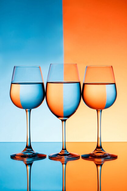 Tre bicchieri di vino con acqua su sfondo blu e arancione.