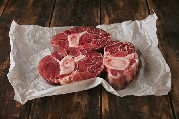 Tre bistecche di carne cruda fresca con osso su carta artigianale bianca dall'alto