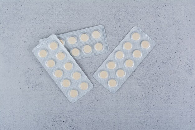 Tre confezioni di pillole medicinali rotonde su sfondo marmo.