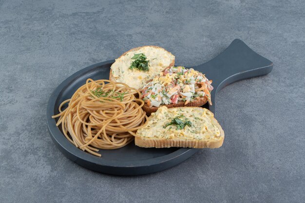 Tre crostini con insalata e spaghetti su tavola nera