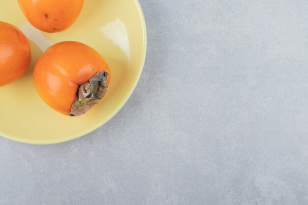 Tre deliziosi cachi sul piatto giallo