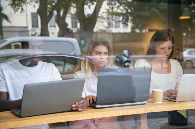 Tre designer che lavorano su laptop dietro la finestra con la riflessione