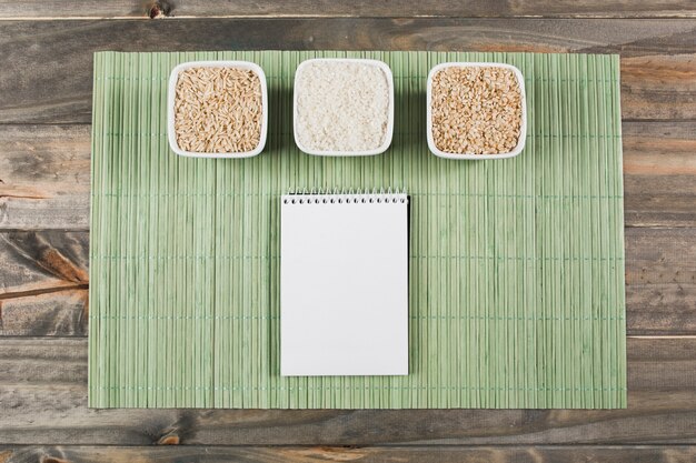 Tre diversi tipi di ciotole di riso non cotte con blocco note a spirale su placemat verde sopra il tavolo