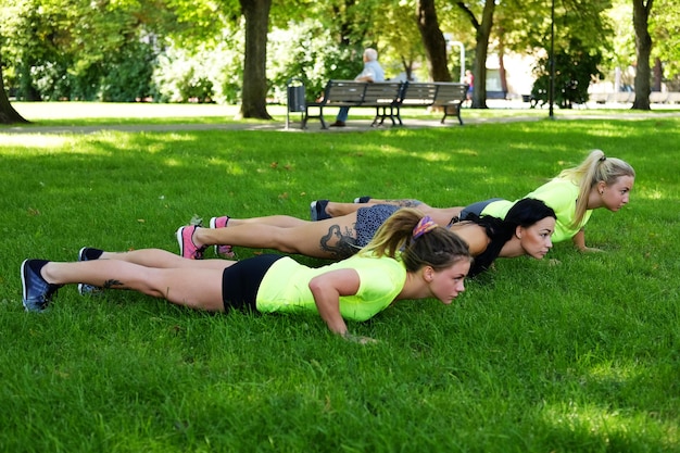 Tre femmine sportive che si scaldano su un prato nel parco estivo.