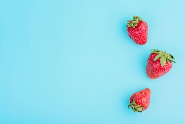 Tre fragole gustose sulla superficie blu