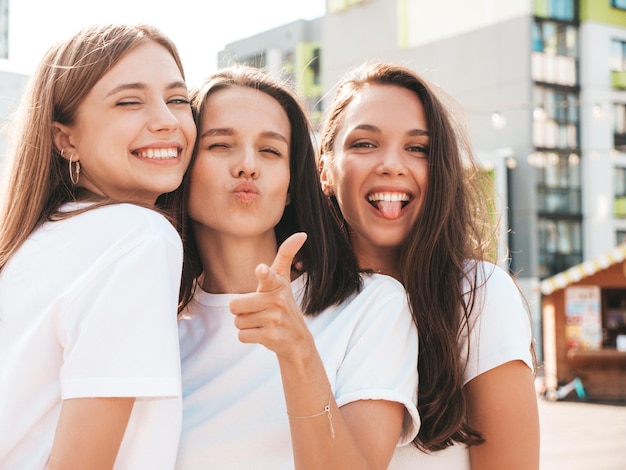 Tre giovani belle donne hipster sorridenti in estate alla moda stessi vestiti Donne sexy spensierate in posa sullo sfondo della stradaModelli positivi che si divertonoAbbracciare Allegri e felici