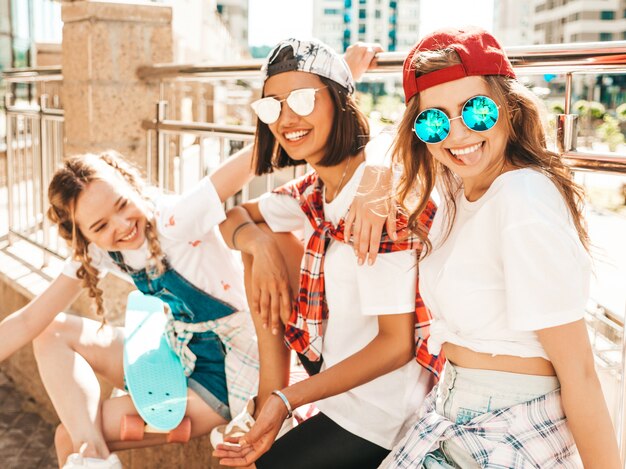 Tre giovani belle ragazze sorridenti con i pattini variopinti del penny.