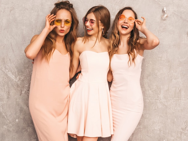 Tre giovani belle ragazze sorridenti in abiti rosa chiaro alla moda estate. Posa sexy spensierata delle donne. Modelli positivi in occhiali da sole rotondi che si divertono