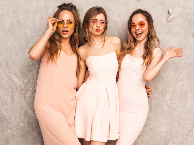 Tre giovani belle ragazze sorridenti in abiti rosa chiaro alla moda estate. Posa sexy spensierata delle donne. Modelli positivi in occhiali da sole rotondi che si divertono