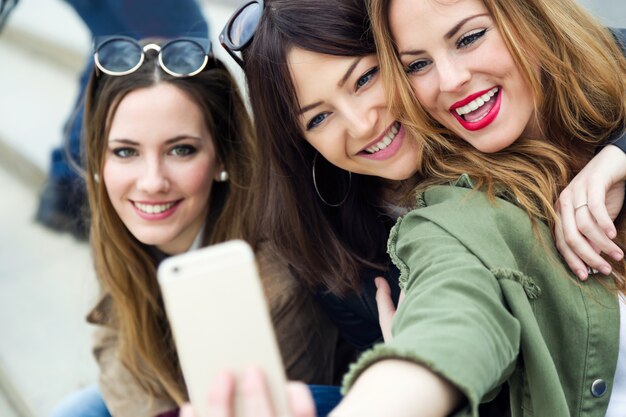 Tre giovani donne che utilizzano un telefono cellulare in strada.