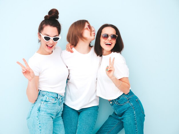 Tre giovani e belle donne hipster sorridenti nella stessa t-shirt bianca estiva alla moda e vestiti di jeans