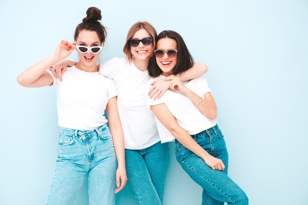 Tre giovani e belle donne hipster sorridenti nella stessa t-shirt bianca estiva alla moda e vestiti di jeans