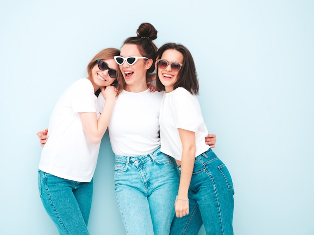 Tre giovani e belle donne hipster sorridenti nella stessa t-shirt bianca estiva alla moda e vestiti di jeans