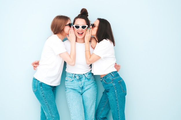 Tre giovani e belle donne hipster sorridenti nella stessa t-shirt bianca estiva alla moda e vestiti di jeans