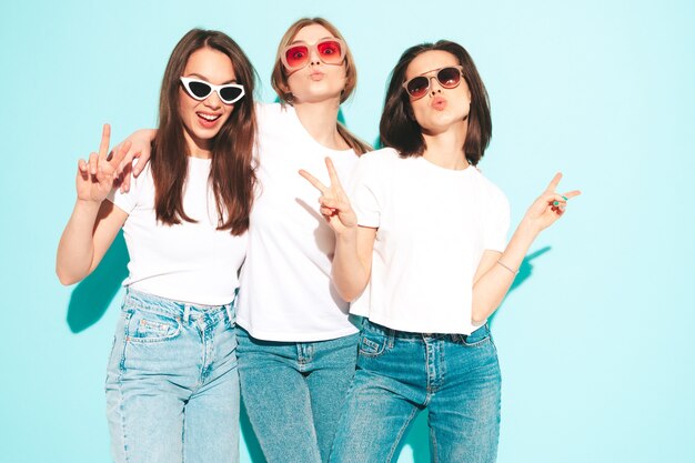 Tre giovani e belle donne hipster sorridenti nella stessa t-shirt bianca estiva alla moda e vestiti di jeans