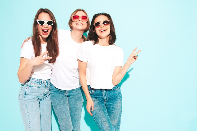 Tre giovani e belle donne hipster sorridenti nella stessa t-shirt bianca estiva alla moda e vestiti di jeans