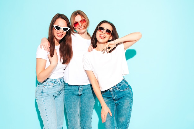 Tre giovani e belle donne hipster sorridenti nella stessa t-shirt bianca estiva alla moda e vestiti di jeans