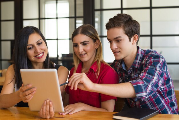 Tre giovani studenti positivi utilizzando la tavoletta digitale nella caffetteria