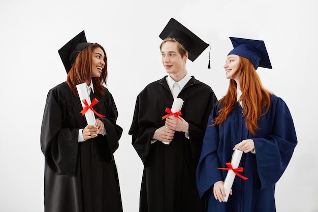 Tre laureati felici che sorridono parlando dei diplomi di tenuta.