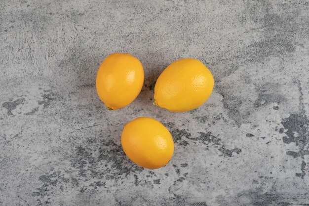 Tre limoni gialli freschi disposti sulla tavola di pietra.