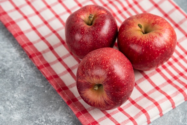 Tre mele rosse con tovaglia a strisce sulla superficie di marmo.