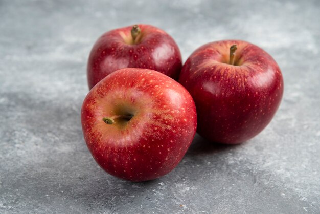 Tre mele rosse mature disposte su una superficie di marmo.