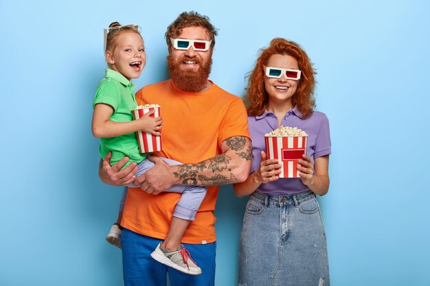 Tre membri della famiglia ottimisti ridono felici, guardano insieme la commedia al cinema, si divertono a mangiare deliziosi popcorn