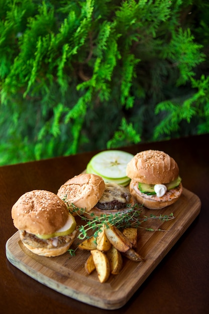 Tre mini hamburger serviti con patatine fritte su tavola di legno