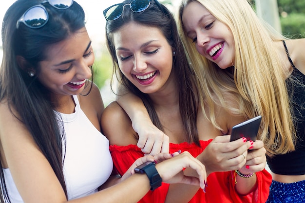 Tre ragazze che chiacchierano con i loro smartphone al parco.