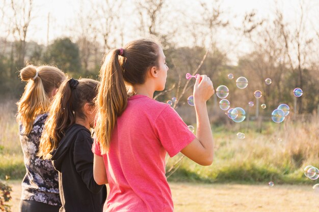 Tre ragazze che soffiano bolla con la bacchetta nel parco