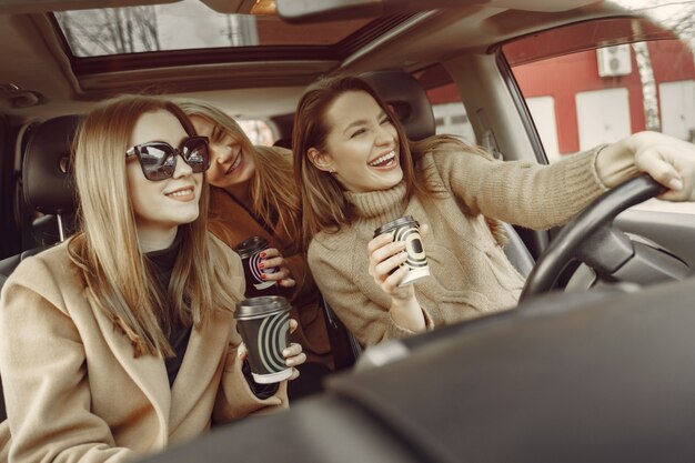 Tre ragazze sedute dentro la macchina e bevendo un caffè