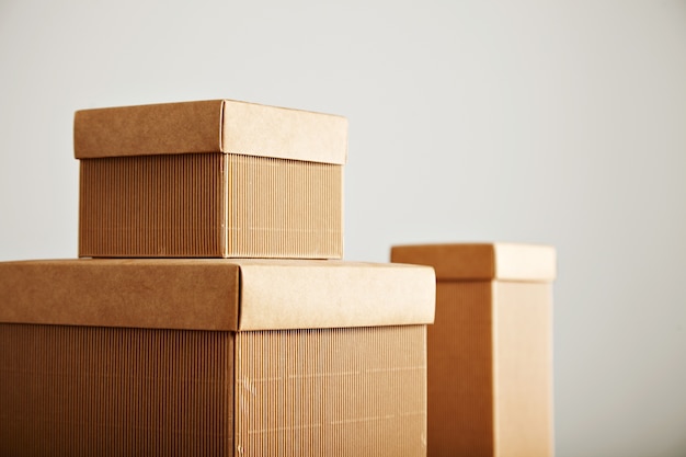 Tre scatole di cartone ondulato beige simili con copertine di diverse forme e dimensioni isolate su bianco