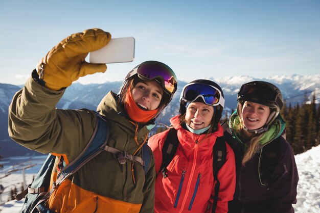 Tre sciatori femminili che prendono selfie sul telefono cellulare
