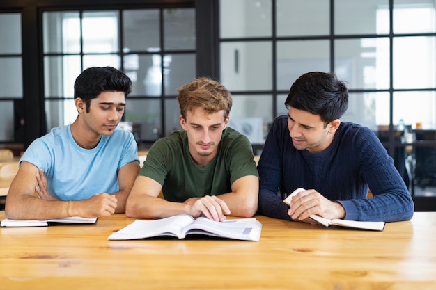 Tre studenti concentrati che leggono i manuali insieme allo scrittorio