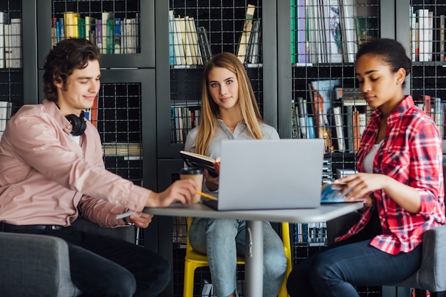 Tre studenti felici che scrivono su quaderni e laptop in biblioteca