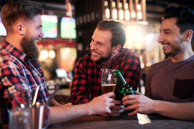 Tre uomini sorridenti che bevono birra al pub