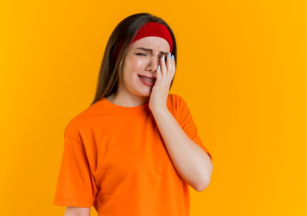 Triste dolorante giovane donna sportiva che indossa la fascia e braccialetti cercando di mettere la mano sul viso