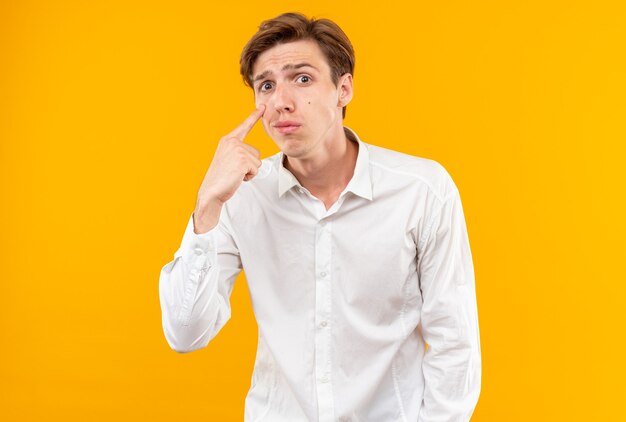 Triste giovane bel ragazzo che indossa una camicia bianca che tira giù la palpebra isolata sul muro arancione