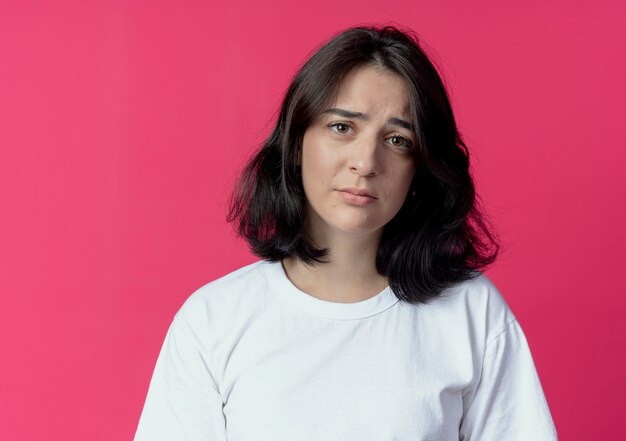 Triste giovane ragazza piuttosto caucasica guardando la telecamera isolata su sfondo cremisi