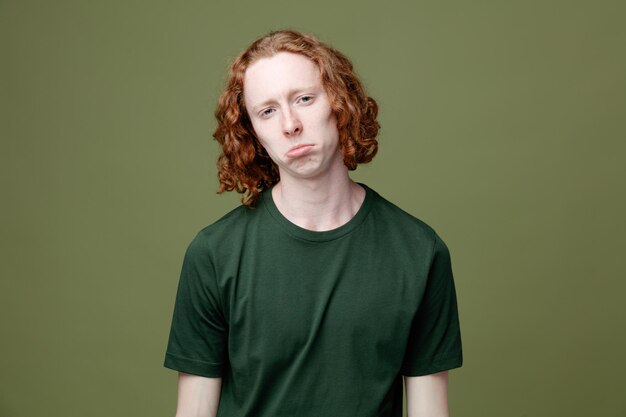 triste guardando la fotocamera giovane bel ragazzo che indossa una maglietta verde isolata su sfondo verde