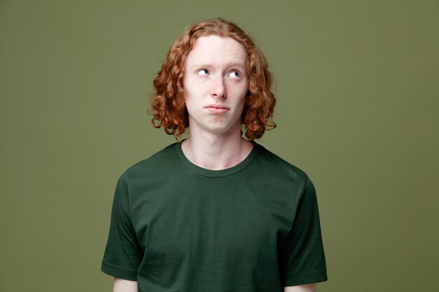Triste guardando lato giovane bel ragazzo che indossa una maglietta verde isolata su sfondo verde