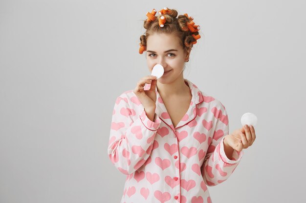 Trucco da decollo ragazza carina prima di dormire con un batuffolo di cotone, indossando bigodini e pigiama