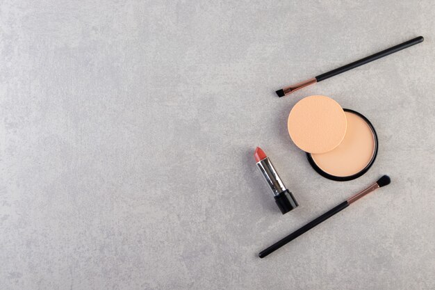 Trucco in polvere in custodia di plastica nera rotonda con rossetto e pennelli.