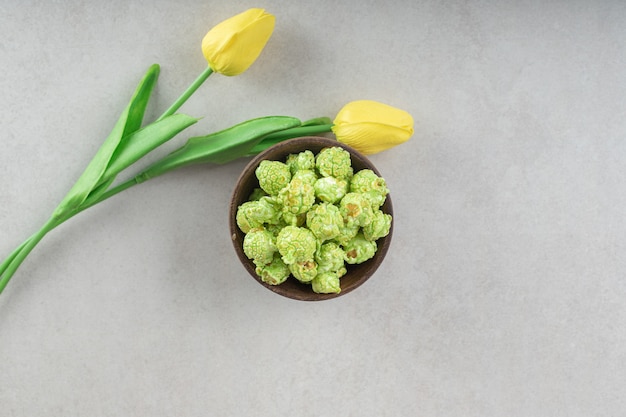 Tulipani gialli profumati posti accanto a una ciotola di caramelle popcorn su marmo.